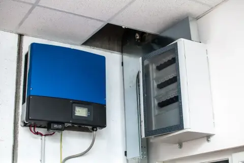 Niebiesko-czarny falownik 1 faza na 3 fazy obok białej skrzynki z bezpiecznikami. Instalacja elektryczna pod sufitem podwieszanym.