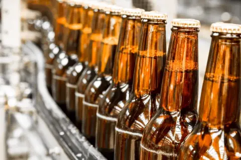 Szklane butelki piwa bezalkoholowego na linii produkcyjnej. Czy piwo bezalkoholowe jest zdrowe? To pytanie nurtuje wielu konsumentów.