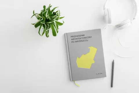 Przewodnik architektoniczny po Wrzeszczu, słuchawki i długopis na białym tle. Zielona roślina w doniczce.