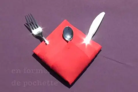 Pliage serviette Noël porte couvert en forme de pochette rouge, avec une fourchette, une cuillère et un couteau.