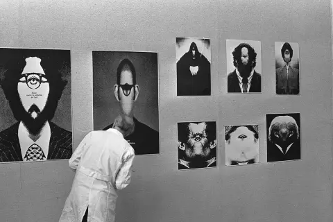 Wystawa prac Romana Cieślewicza. Czarno-białe portrety o surrealistycznych twarzach, jedna osoba w białej fartuchu ogląda ekspozycję.