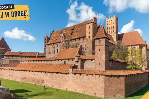 Potężny zamek w Malborku, z czerwonej cegły, z licznymi wieżami i murami obronnymi, na tle błękitnego nieba z chmurami.