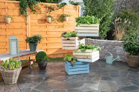 Fioriere in legno fai da te impilate, piene di verdure fresche, creano un angolo verde su un patio in pietra.