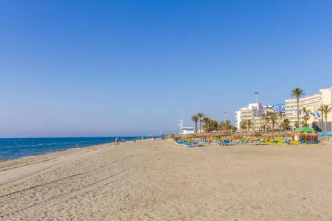 Amplia playa de la urbanización de Roquetas con sombrillas, tumbonas y edificios hoteleros al fondo.