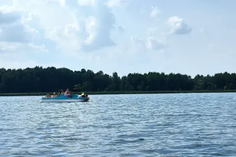 Rodzina pływa rowerkiem wodnym po spokojnym jeziorze Białka Lubelskie. W tle zielony las i błękitne niebo z chmurami.