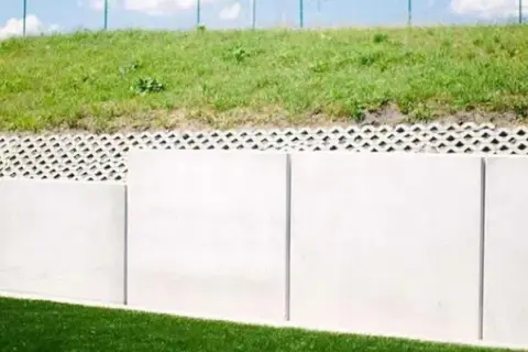 Nowy mur oporowy odległość od granicy działki. Betonowe płyty i ażurowa warstwa pod zielonym nasypem.