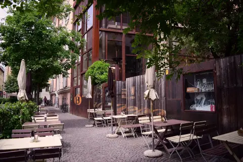 Tavoli all'aperto e ombrelloni di fronte al Batzen Bräu, con un'architettura industriale e un'atmosfera rilassata.