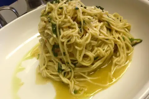 Un piatto di spaghetti aglio olio e peperoncino cremosi, conditi con prezzemolo fresco e un filo d'olio d'oliva.