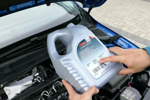 Osoba trzymająca kanister oleju silnikowego TITAN GT1 PRO C-3 SAE 5W-30 nad silnikiem. Czy można mieszać oleje silnikowe? Sprawdź specyfikację!