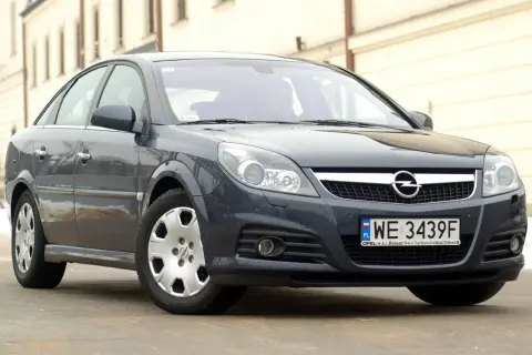 Ciemnoszary Opel Vectra C z polskimi tablicami WE 3439F. Widać jego przednie reflektory, atrapę chłodnicy z logo Opla i zderzak.