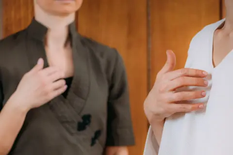 Zwei Frauen üben Klopftechnik zur Linderung von Angst. Eine hält die Hand auf der Brust, die andere auf dem Oberarm.