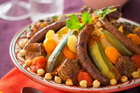 Un plat généreux de couscous royal, garni de merguez, de morceaux de viande, de légumes et de pois chiches, prêt à être dégusté.