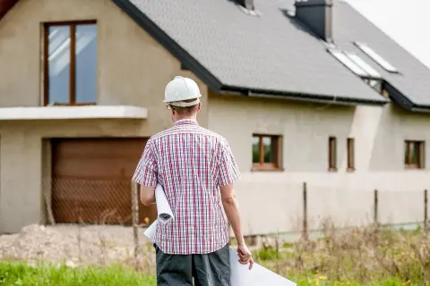 Inżynier w kasku nadzoruje budowę domu, trzymając plany.