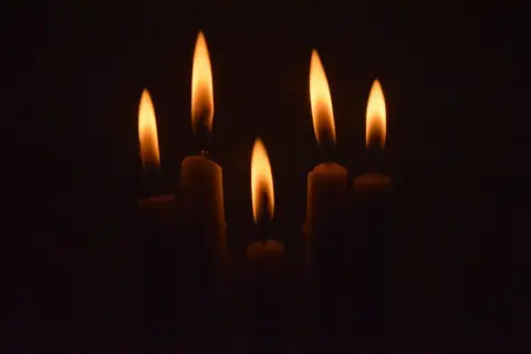 Płomienie świec w ciemności, symbolizujące zablokowaną żałobę.
