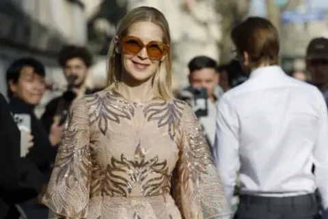 Donna con abito scintillante e occhiali da sole oversize, perfetta per un dress code cocktail donna.