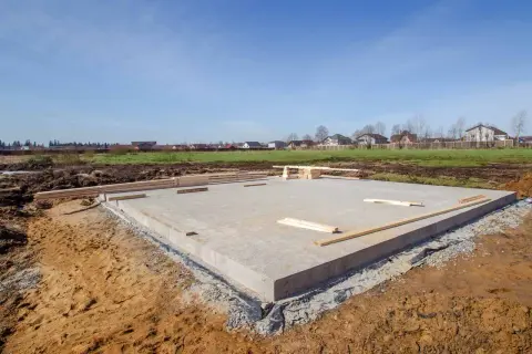Płyta fundamentowa, jeden z rodzajów fundamentów, gotowa pod budowę domu. W tle widać domy i zielone pola.