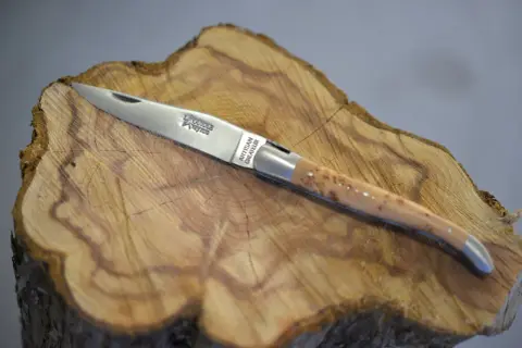 Navaja Laguiole artesanal, con mango de madera veteada y detalles plateados, reposa sobre un tocón de árbol.
