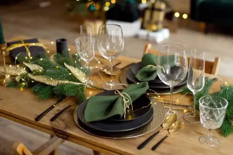 Table dressée pour Noël avec pliage serviette avec rond de serviette, guirlande lumineuse et branches de sapin.