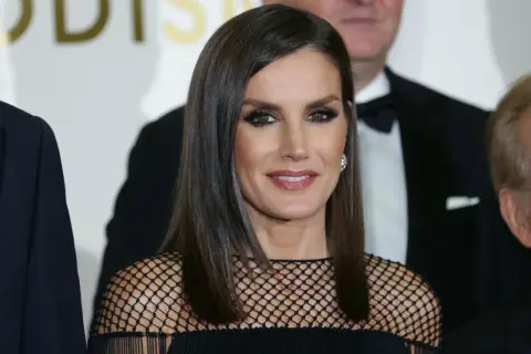 Elegancka królowa Letizia w czarnej, siateczkowej kreacji, z błyszczącymi oczami i uśmiechem, pozuje do zdjęcia z innymi osobami.