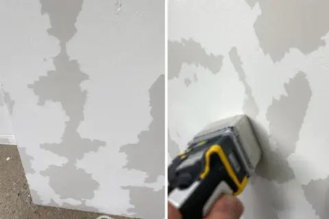 Le mur en toile de verre présente des zones abîmées, comme des taches d'humidité. Un outil est utilisé pour évaluer les dégâts.