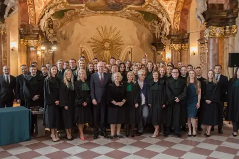 Grupa prawników w togach stoi w ozdobnym wnętrzu.