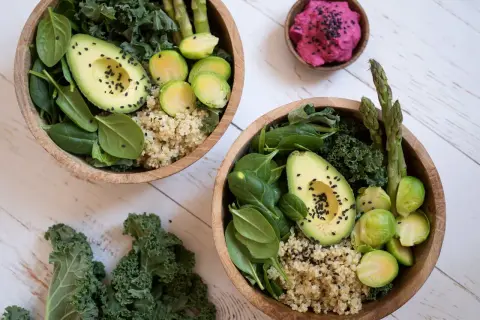 Två skålar med nyttig mat: quinoa, spenat, grönkål, avokado, brysselkål och sparris. En liten skål med rosa röra.