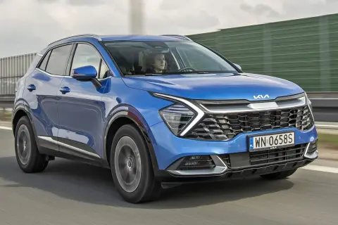 Niebieska, nowa Kia Sportage z kierowcą za kierownicą jedzie po drodze.