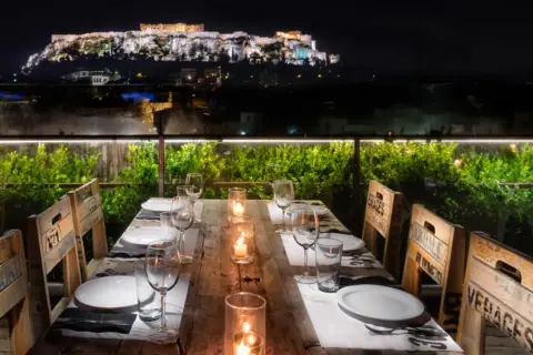 Gedeckter Tisch mit Blick auf die beleuchtete Akropolis bei Nacht.
