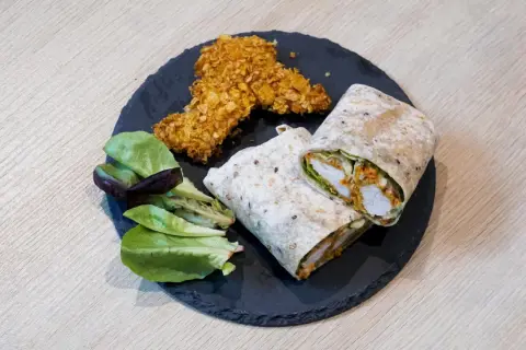 Pyszny kebab w tortilli, idealnie zawinięty, z chrupiącymi kawałkami kurczaka i świeżą sałatką.