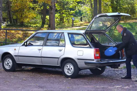 Man lastar en blå frisbee i bakluckan på en silverfärgad Renault 18 kombi i höstlandskap.