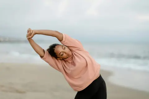 Femme en posture qi gong, s'étirant sur la plage au lever du soleil.