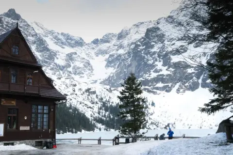 Maison en bois au pied des montagnes enneigées des Tatras en Pologne. Un lac gelé s'étend devant.