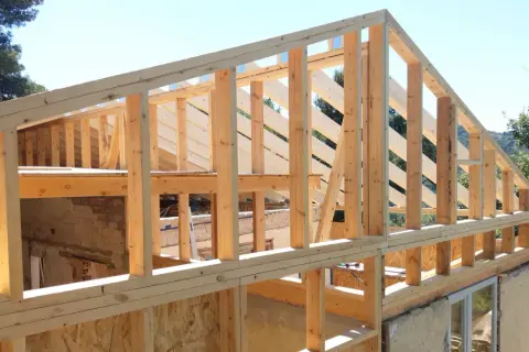 Estructura de madera para casa en construcción, con vigas y pilares de madera a la vista bajo un cielo azul.