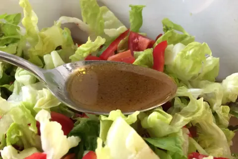 Löffel mit Balsamico Dressing über frischem Salat mit Tomaten und Paprika.