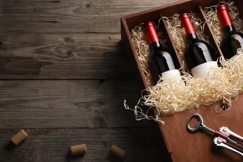 Drewniana skrzynka z trzema butelkami marani wino półsłodkie, wypełniona słomą. Obok korkociąg i korki.