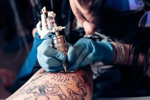 Artista creando un tatuaje de arte negro en la pierna.