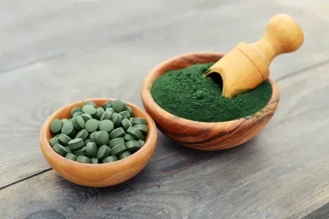 Chlorella i spirulina efekty: zielone tabletki i proszek w drewnianych miseczkach, gotowe do spożycia dla zdrowia.
