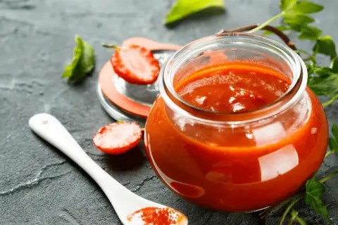 Un pot de ketchup maison, garni de fraises et de feuilles vertes, sur fond sombre.
