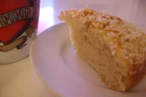En bit gammaldags kardemummakaka med nötter på en vit tallrik, bredvid en mugg med texten "MAMMA".