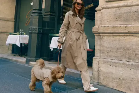 Elegancka kobieta w beżowym płaszczu, idealnym przykładzie, jak nosić płaszcz damski, spaceruje z psem po ulicy.