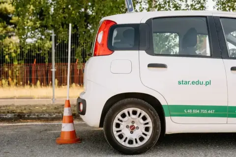 Szukasz informacji, ile kosztuje prawo jazdy AM? Na zdjęciu biały samochód szkoleniowy z numerem telefonu i adresem strony internetowej szkoły jazdy.
