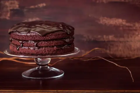 Torta a tre strati di torte al cioccolato, ricoperta da glassa lucida al cioccolato, su un'alzata di vetro.