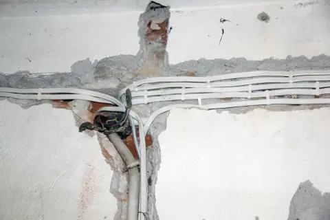 Widoczne przewody elektryczne w peszlach, częściowo ukryte w bruzdach w ścianie. Instalacja aluminiowa w trakcie prac.