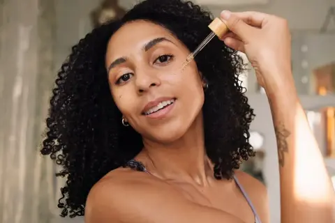 Frauen mit lockigem Haar tragen ein Serum mit Peptiden auf, um ihre Haut mit Feuchtigkeit zu versorgen.
