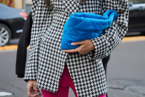 Elegancka marynarka w pepitkę, zestawiona z jaskrawymi różowymi spodniami i błękitną kopertówką, tworzy modne stylizacje.