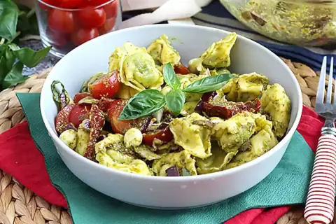 Tortellini z pesto, pomidorkami koktajlowymi i bazylią w białej misce.