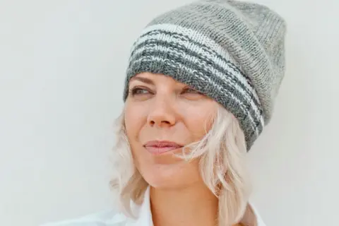 Frau mit blonden Haaren und Strickmütze, die nachdenklich in die Ferne blickt. Sie genießt ihr Leben mit 55 in Rente.