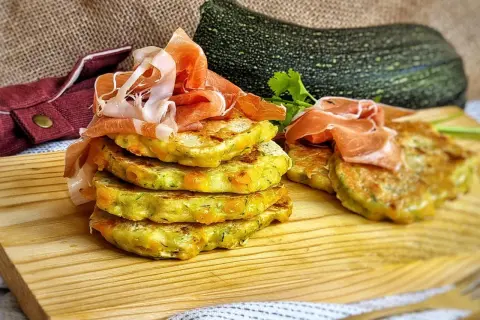 Deliciosas tortillitas de calabacín apiladas, coronadas con jamón serrano. Un plato fresco y sabroso.