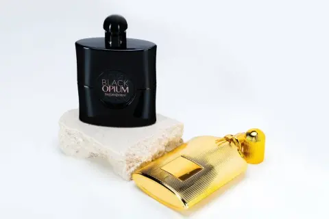 Elegancki flakon Black Opium 90 ml na kamiennej podstawie obok złotego flakonu.