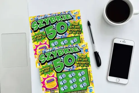 Dwie zdrapki "Szybkie 50" leżą obok laptopa, telefonu i kawy. Dowiedz się, jak sprawdzić zdrapkę i czy masz szczęście!